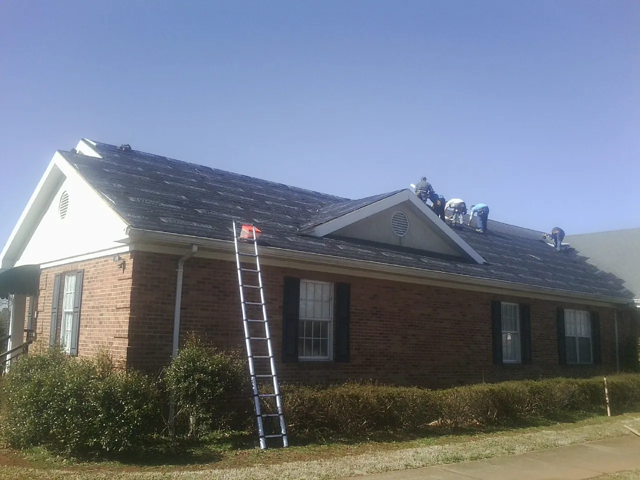 Crew tearing shingles off a brick ranch roof with a ladder set — Emergency Roof Repair work by our crew in Villa Rica