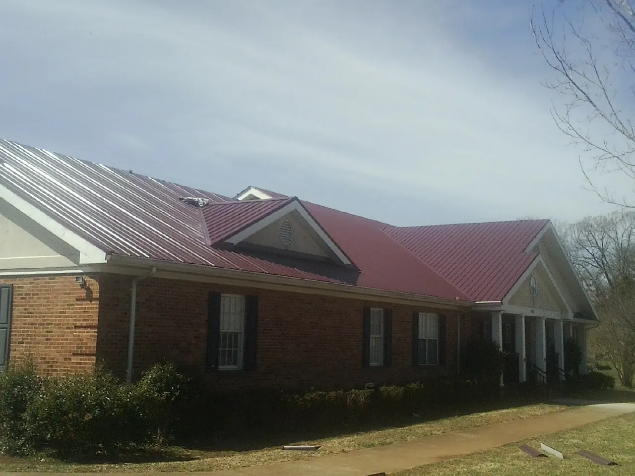 Red metal roof with gabled entries on a long brick building, from a Hail Damage Roof Repair job in Villa Rica