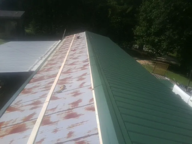 Old rusted panels beside newly installed green metal roofing — Wind Damage Roof Repair by Roofing Brothers in Villa Rica
