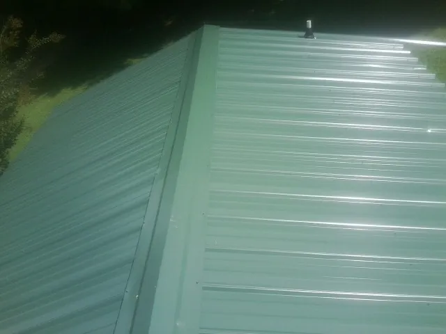 New green metal panels meeting at the ridge of a roof — Flat Roof Repair work by our crew in Villa Rica