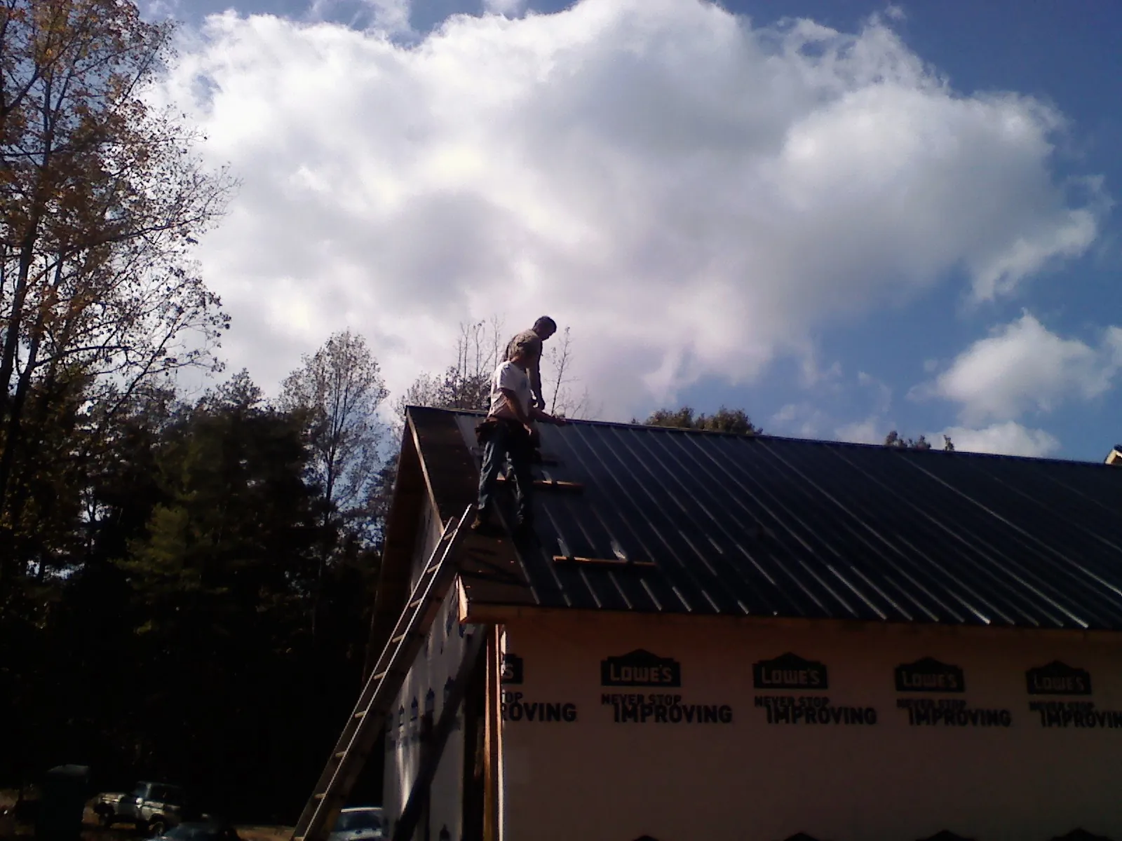 Roofer fastening dark metal panels high against a cloudy sky, from a Roof Inspection job in Villa Rica