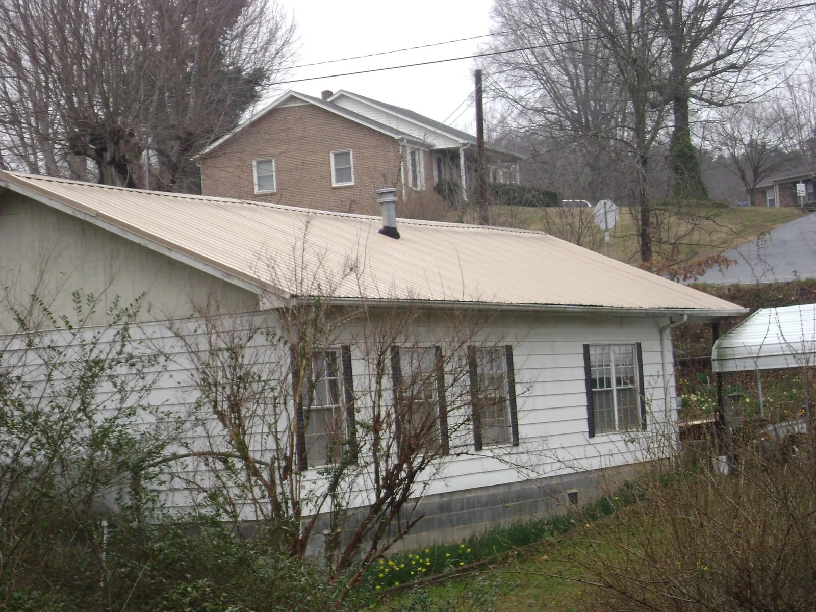Tan metal roof on a white sided house set into a hillside — Commercial Roofing by Roofing Brothers in Villa Rica