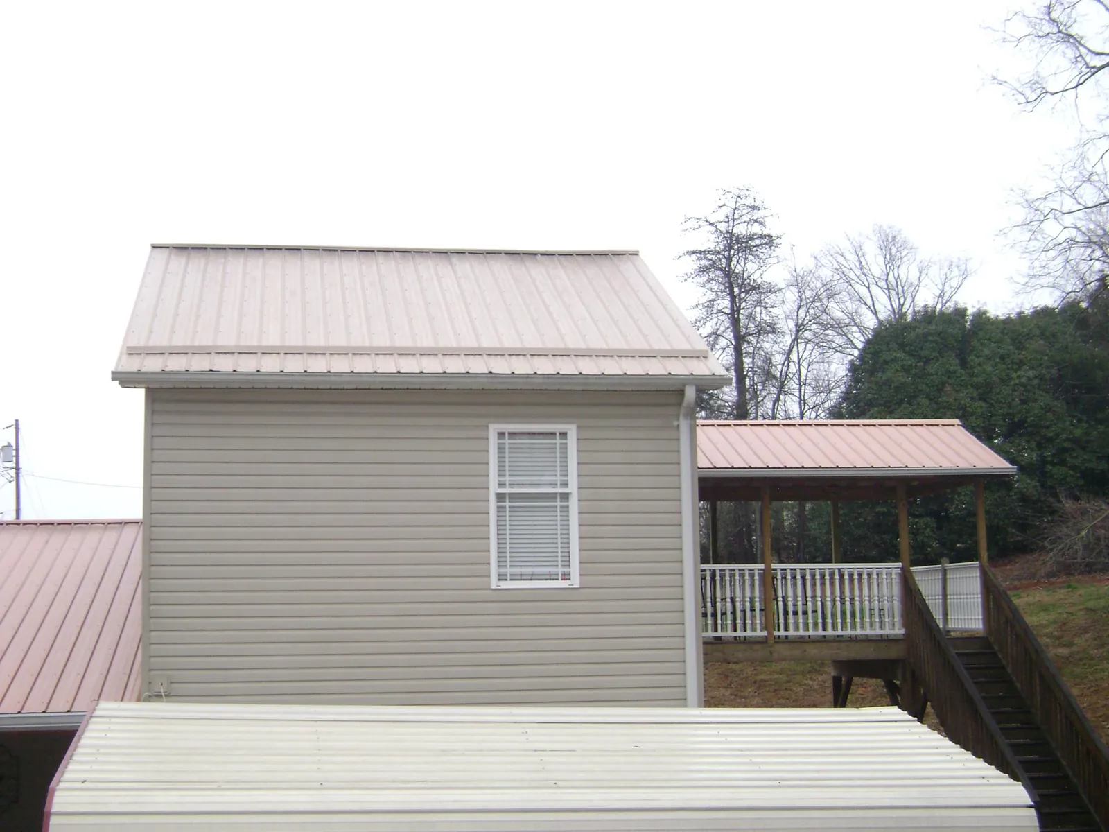 Tan metal roofs on a two story addition and attached porch, from a Roof Replacement job in Villa Rica